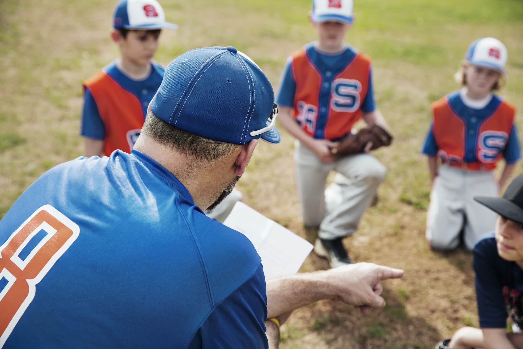 Rear View Of Coach Pointing While Discussing With Baseball Team On Field